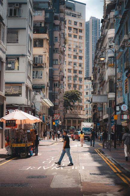 Daytime scene of a busy street in Hong Kong with pedestrians and urban environment.
