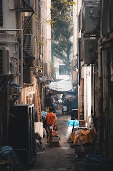 Urban alleyway scene with a worker carrying boxes in Hong Kong.