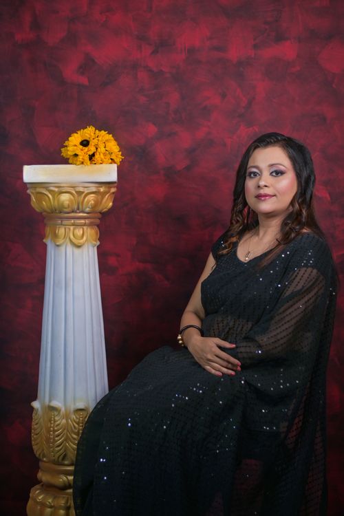 Free Portrait of a woman in a black saree, sitting next to a decorative column with sunflowers. Stock Photo