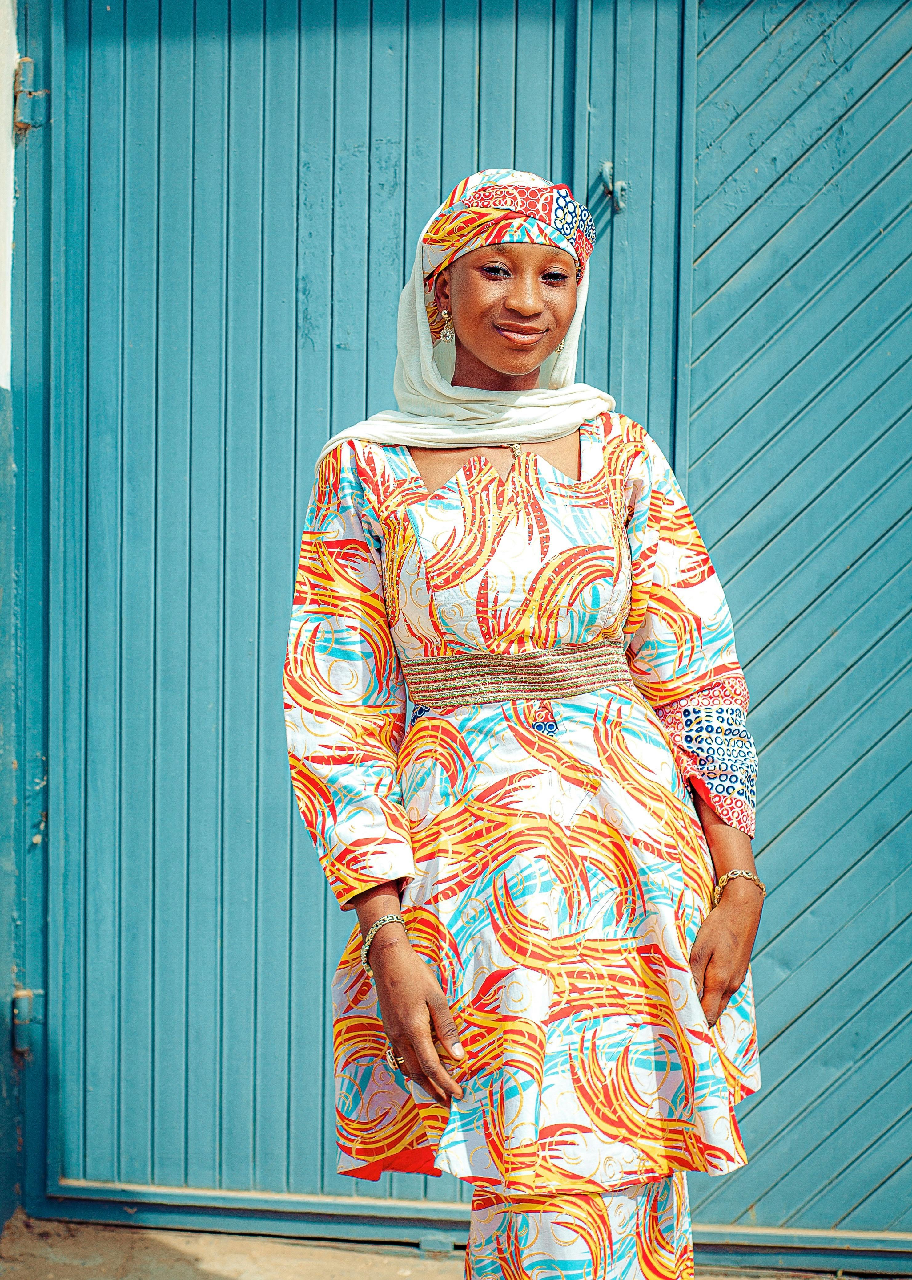 De franc Dona africana amb vestit tradicional vibrant posant a l'aire lliure contra una porta blava. Foto d'estoc