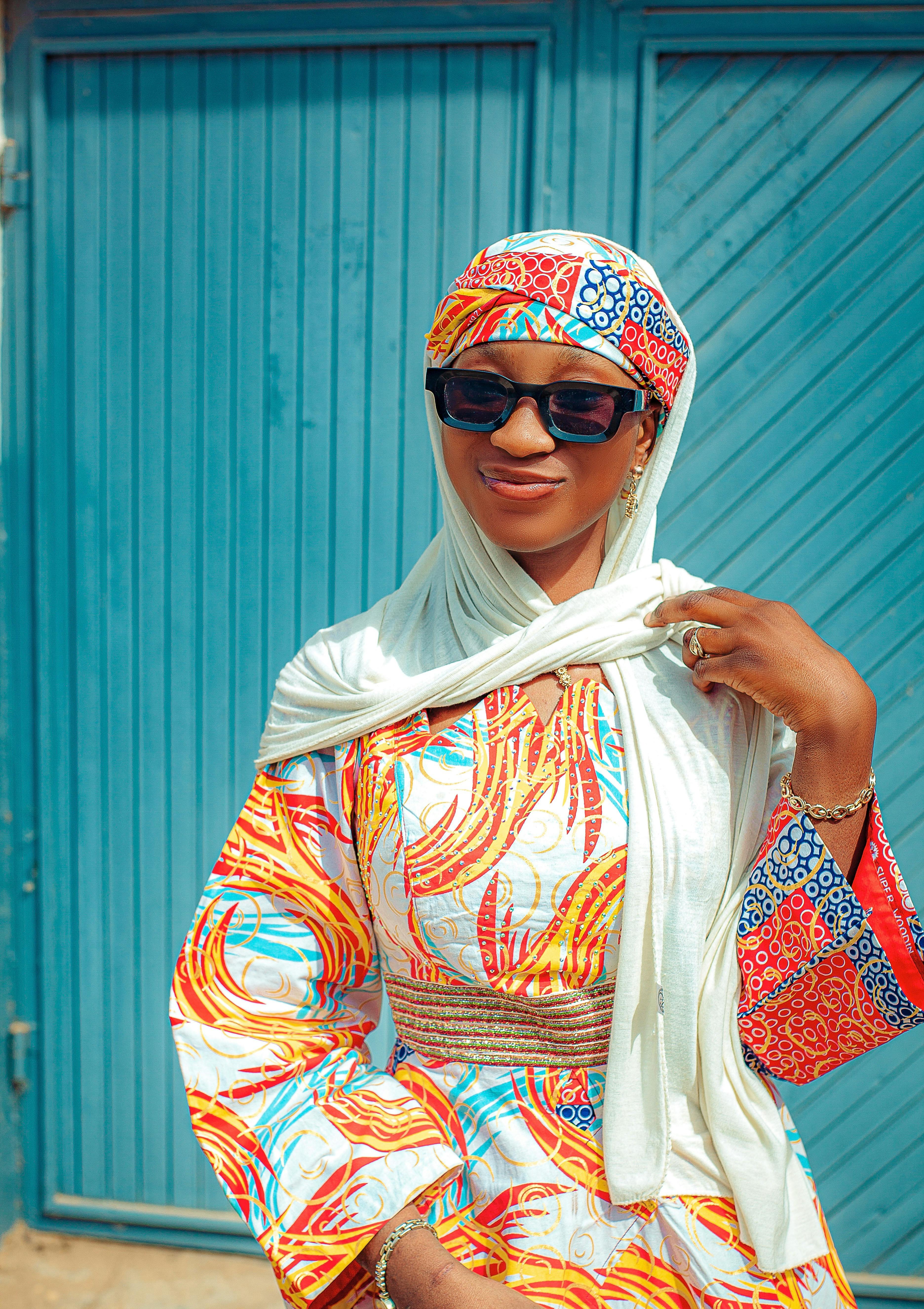 De franc Dona africana elegant amb vestit tradicional vibrant i ulleres de sol, posant amb confiança. Foto d'estoc