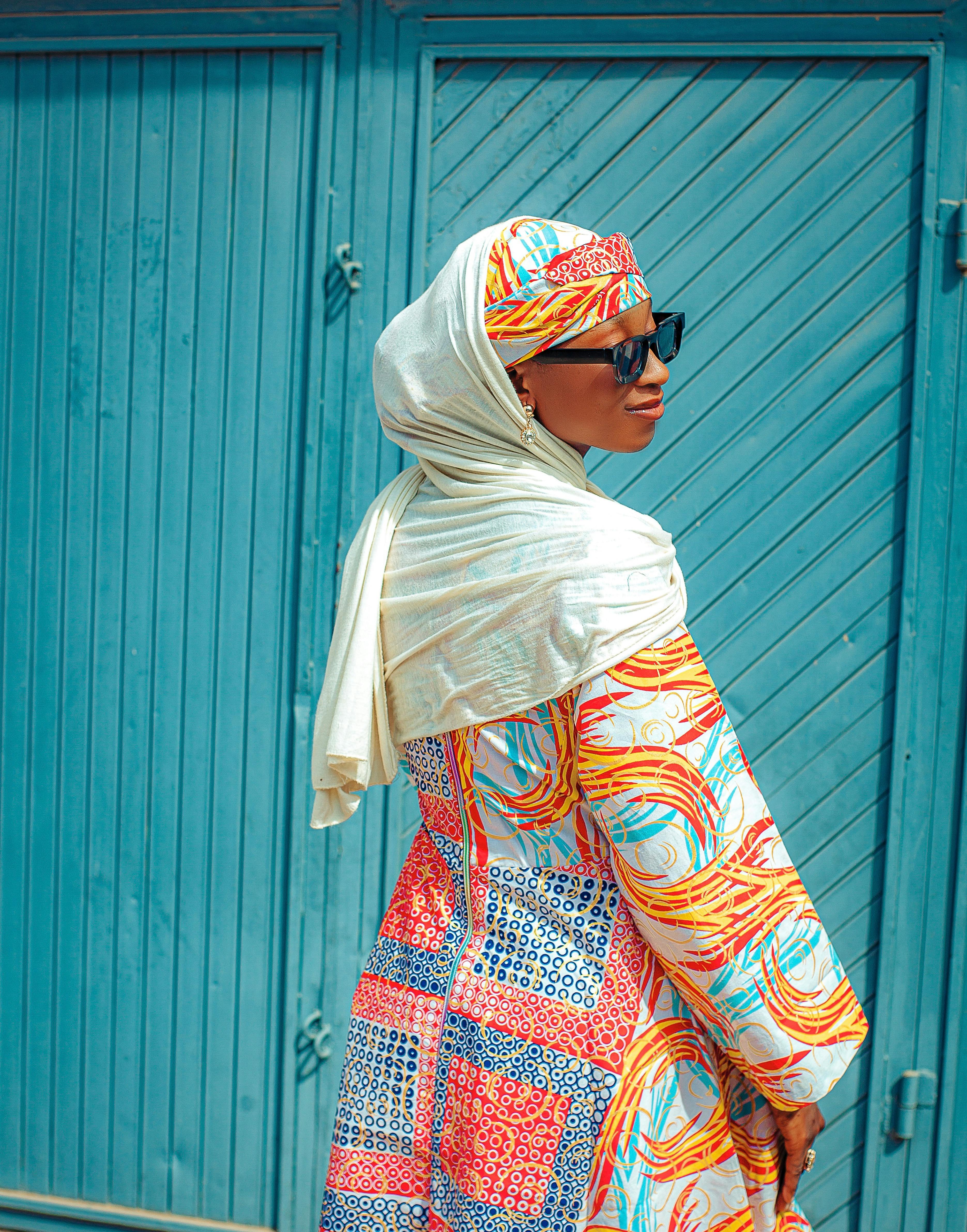 De franc Dona elegant amb vestit vibrant i mocador al cap posa contra la porta blava a l'exterior. Foto d'estoc