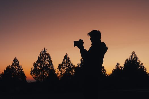 A silhouette of a photographer capturing the sunrise against a scenic forest backdrop.