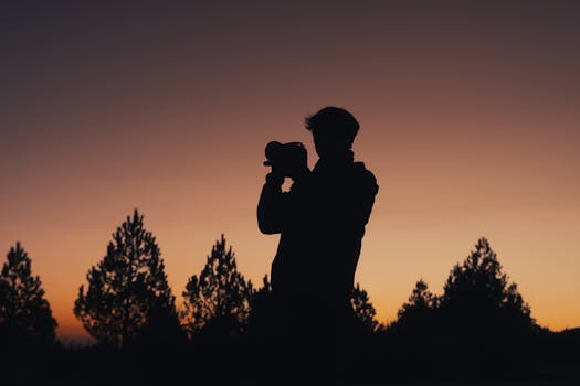 Silhouette of a photographer capturing the twilight sky with trees in the background.