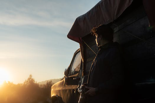 Photographer with camera at sunrise by a truck in a forest setting.