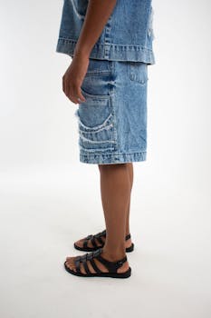 Side view of a person wearing a denim outfit and sandals on a white background.