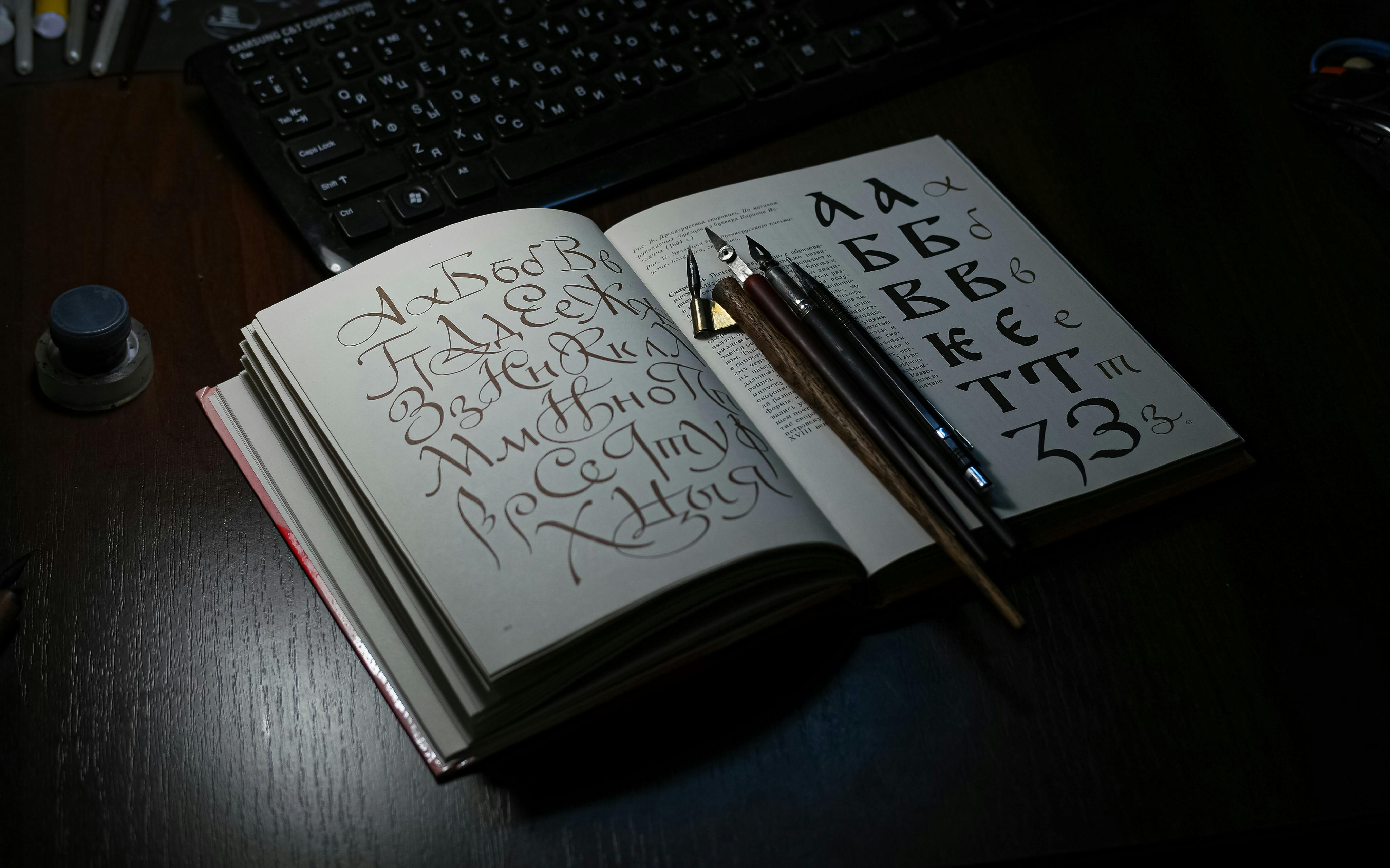 Free Open book showing Cyrillic calligraphy with quill pens on a desk, ideal for art and language themes. Stock Photo