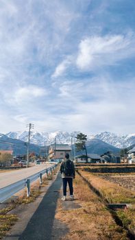 A person walks along a rural path towards beautiful snow-covered mountains on a clear day.