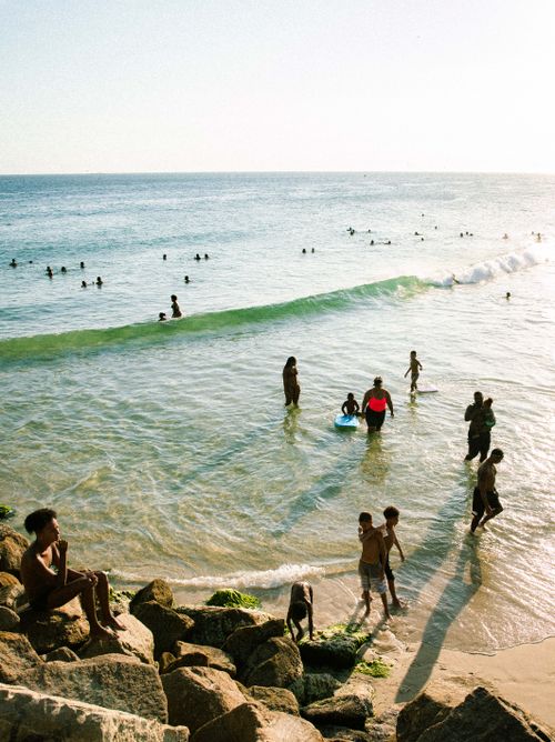 Free A vibrant beach scene with people swimming and relaxing in the ocean under the sun. Stock Photo