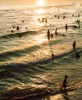 Silhouetted people enjoying the beach waves at sunset, creating a peaceful and vibrant scene.