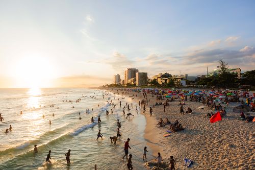 Free A lively beach scene in Rio de Janeiro at sunset, with people enjoying the water and sand. Stock Photo