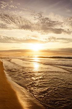Peaceful sunrise over ocean waves and sandy beach, creating a tranquil seascape.