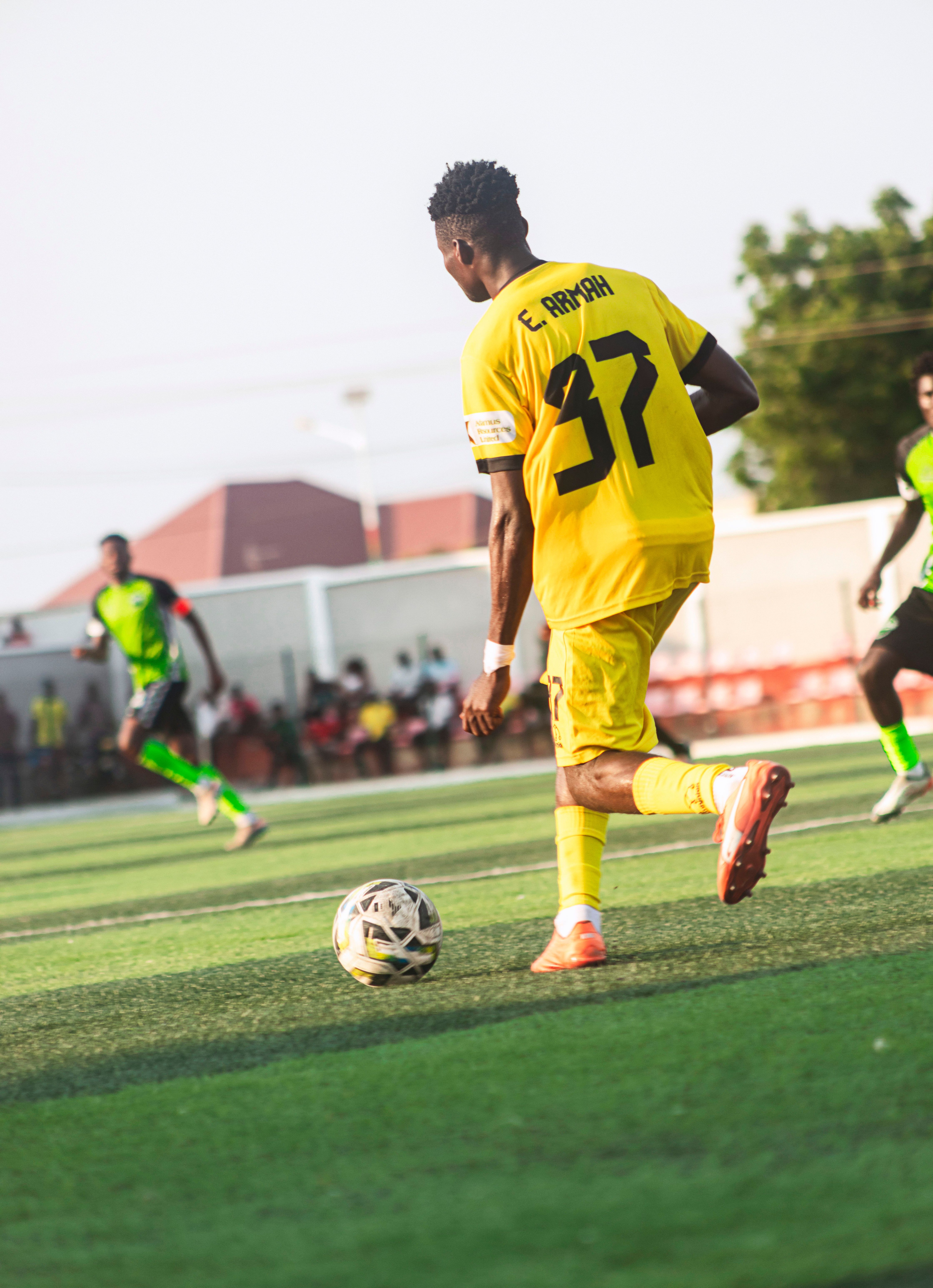 Dynamic action shot of a soccer player in yellow on the field during a sunny day match.
