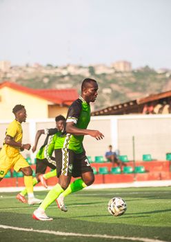 Youth football match with players in vibrant uniforms running on field under sunny sky.