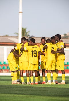 A soccer team in yellow jerseys gathers in a huddle on an outdoor field.