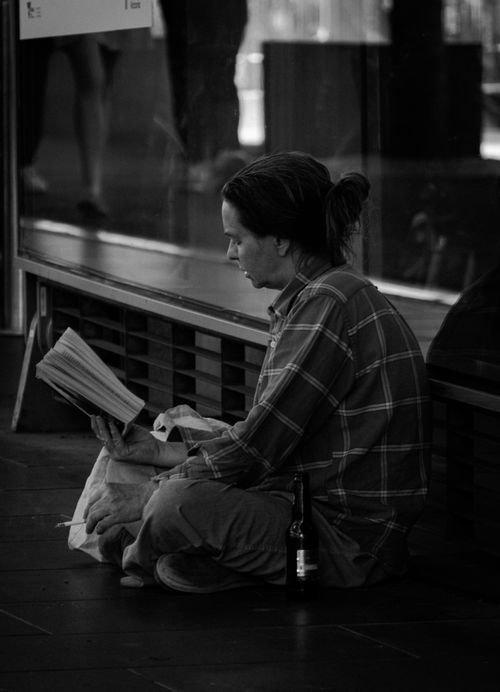 Free A black and white image of a man sitting on the floor indoors, engrossed in a newspaper. Stock Photo