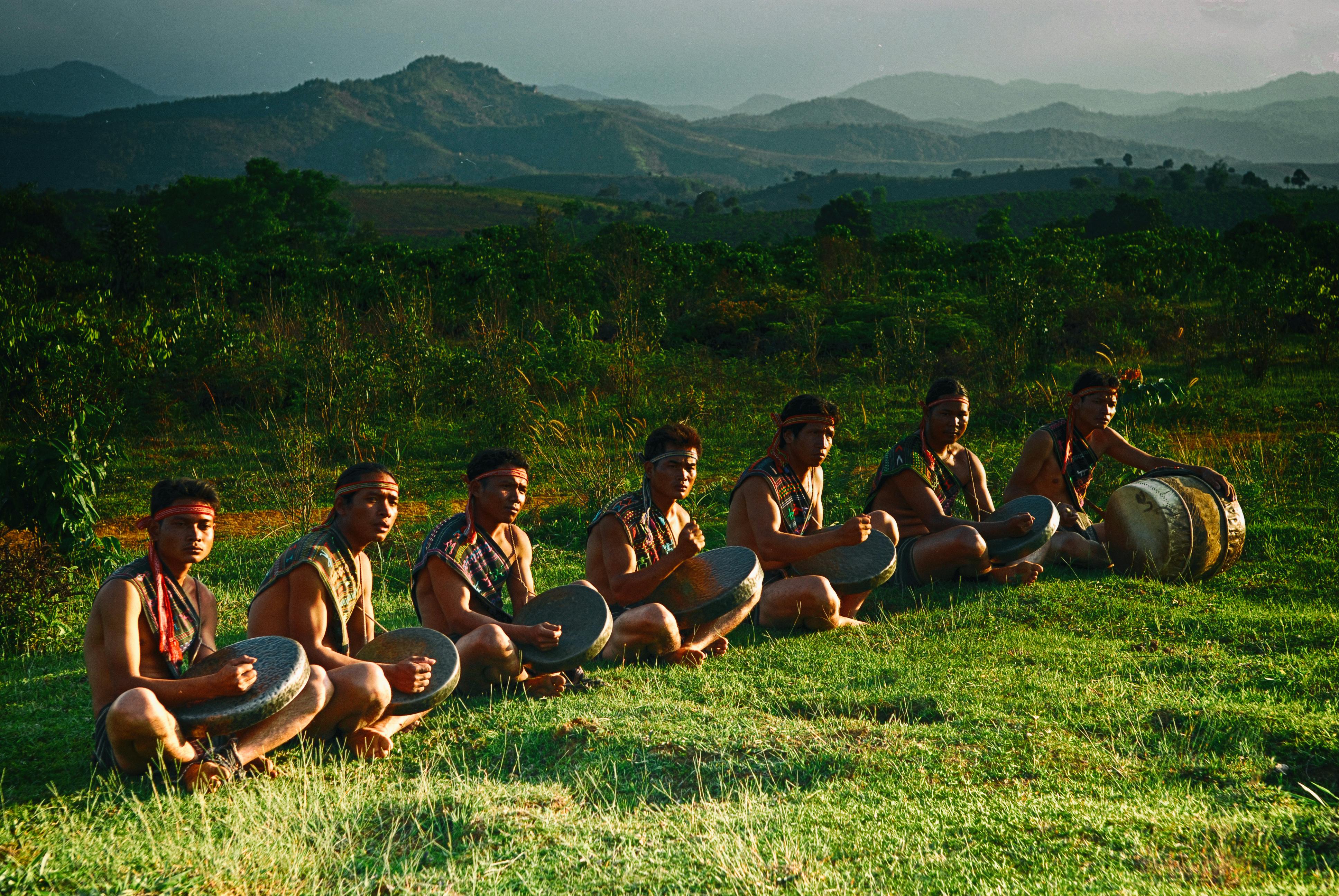 Group of men playing traditional drums in a scenic hilly landscape during the day.