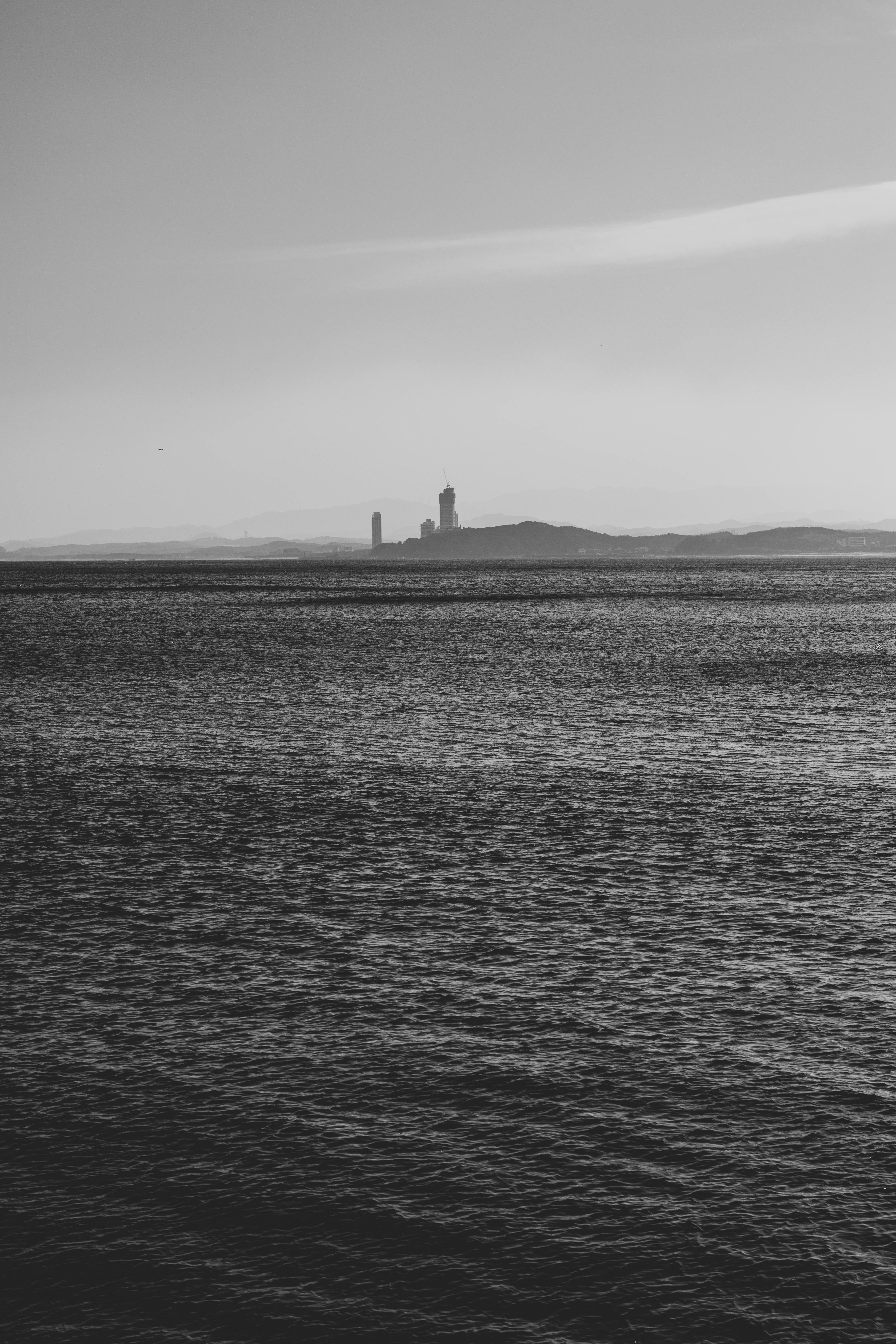grátis Farol distante em uma ilha rochosa em um vasto oceano, capturado em monocromático. Foto profissional