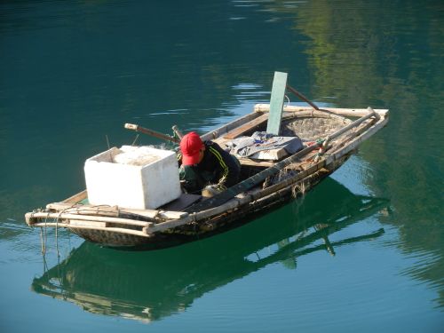 Free A fisherman working alone in a traditional wooden boat on calm waters. Stock Photo