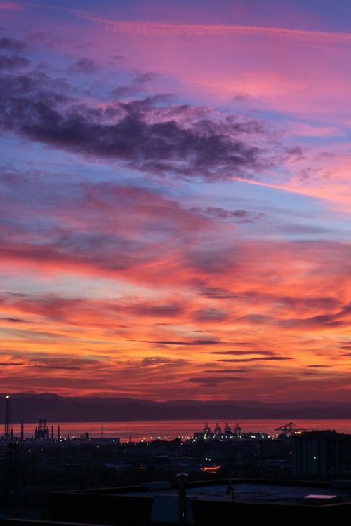 Free A stunning sunset with vibrant colors over an industrial harbor skyline. Stock Photo