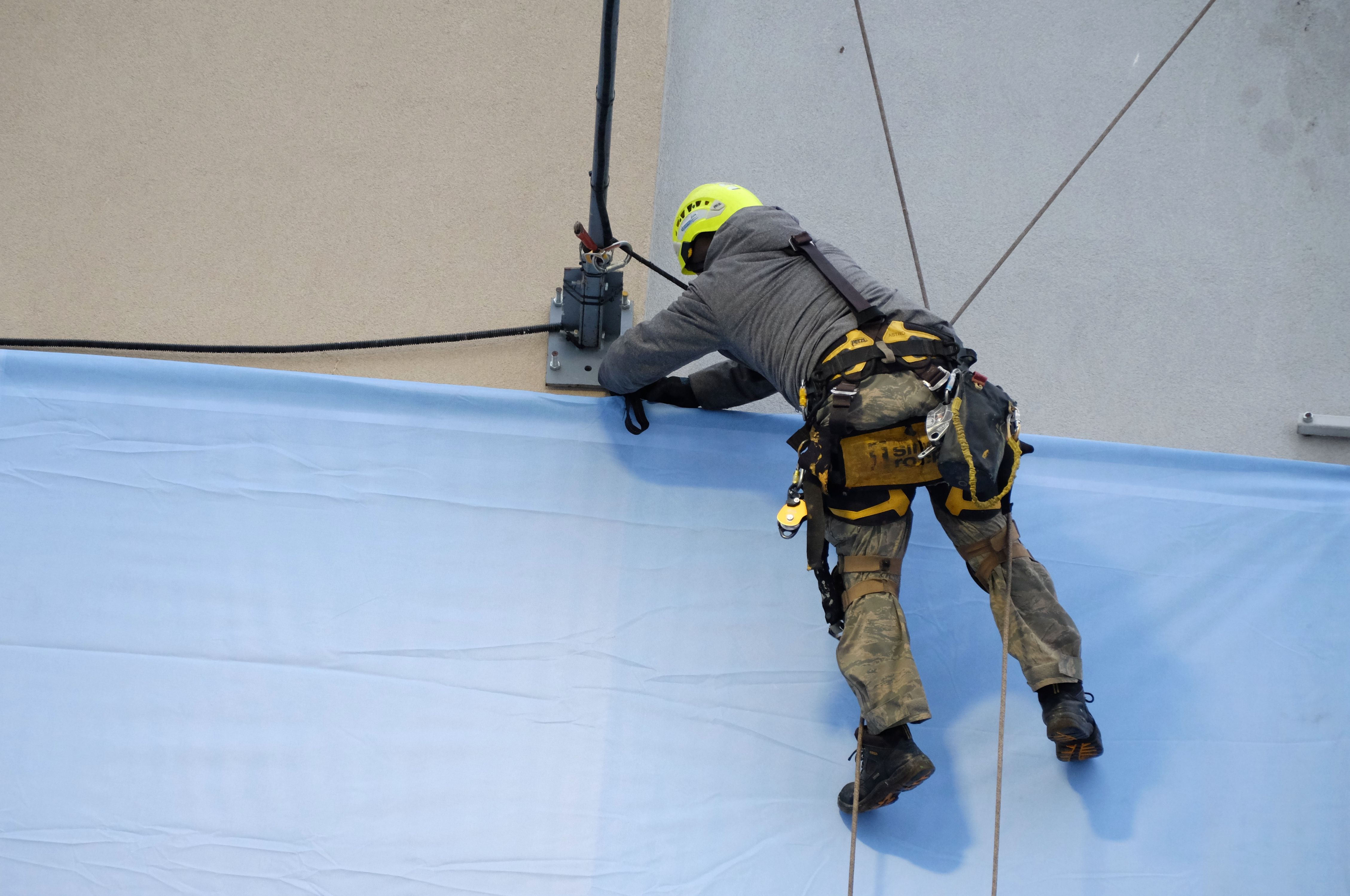 Rope Access Technician Fixing Banner on Building · Free Stock Photo