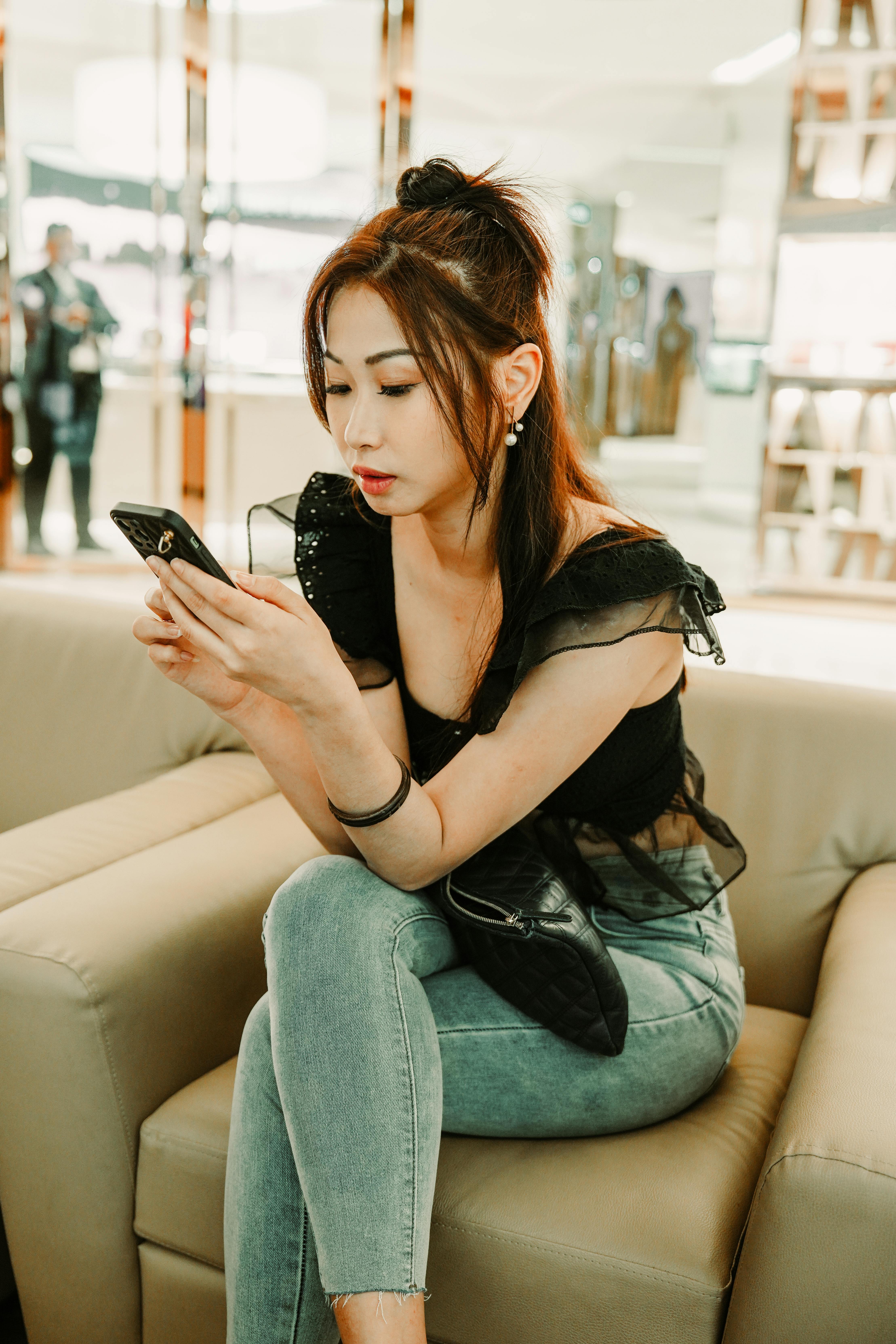 무료 세련된 젊은 여성이 모던한 라운지에 앉아 스마트폰으로 문자를 보내고 있다. 그녀는 캐주얼하면서도 시크한 복장을 하고 있다. 스톡 사진