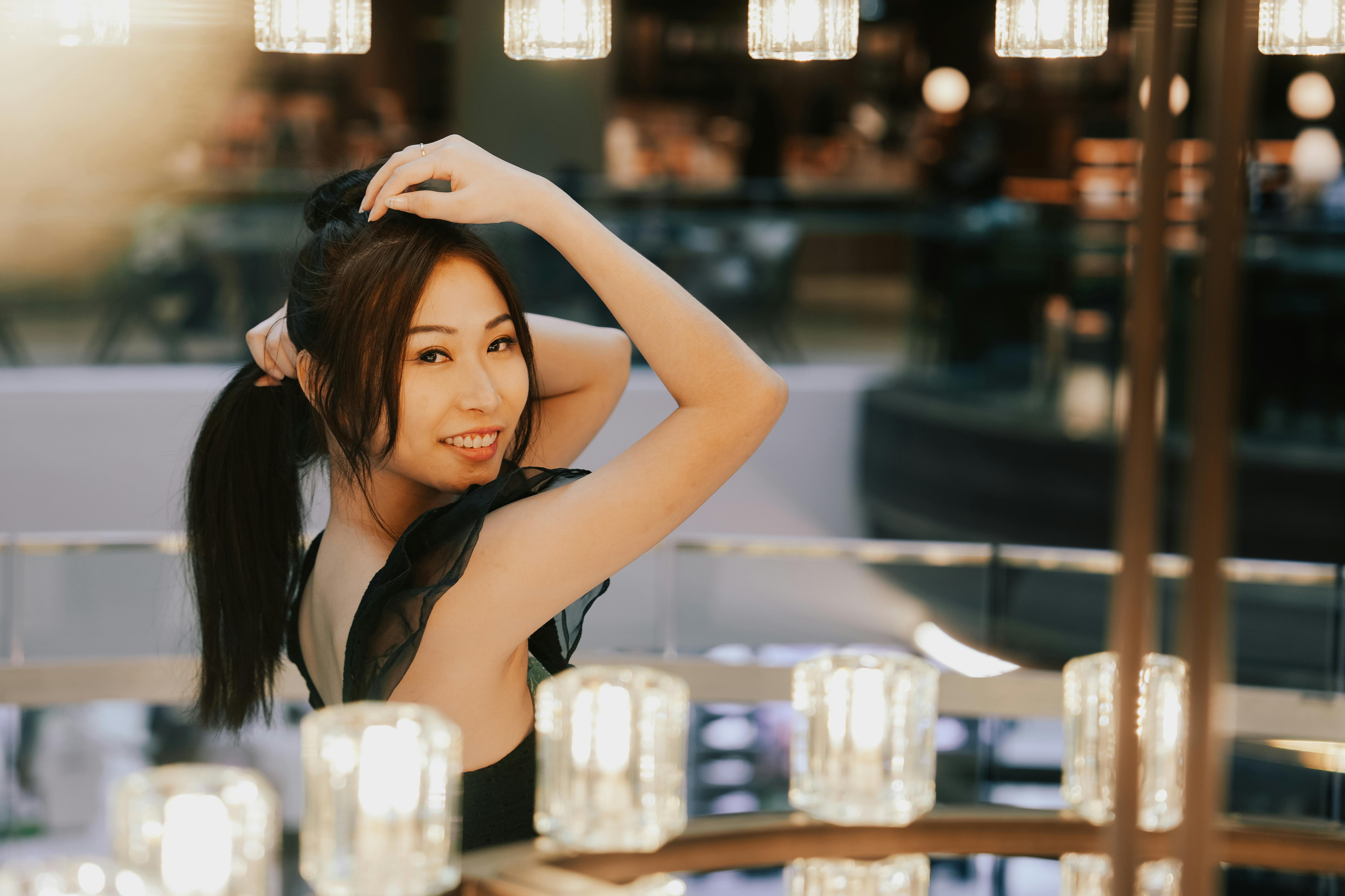 Безкоштовне Молода жінка посміхається, позуючи в приміщенні з теплим розсіяним освітленням, створюючи яскраву та радісну атмосферу. стокове фото