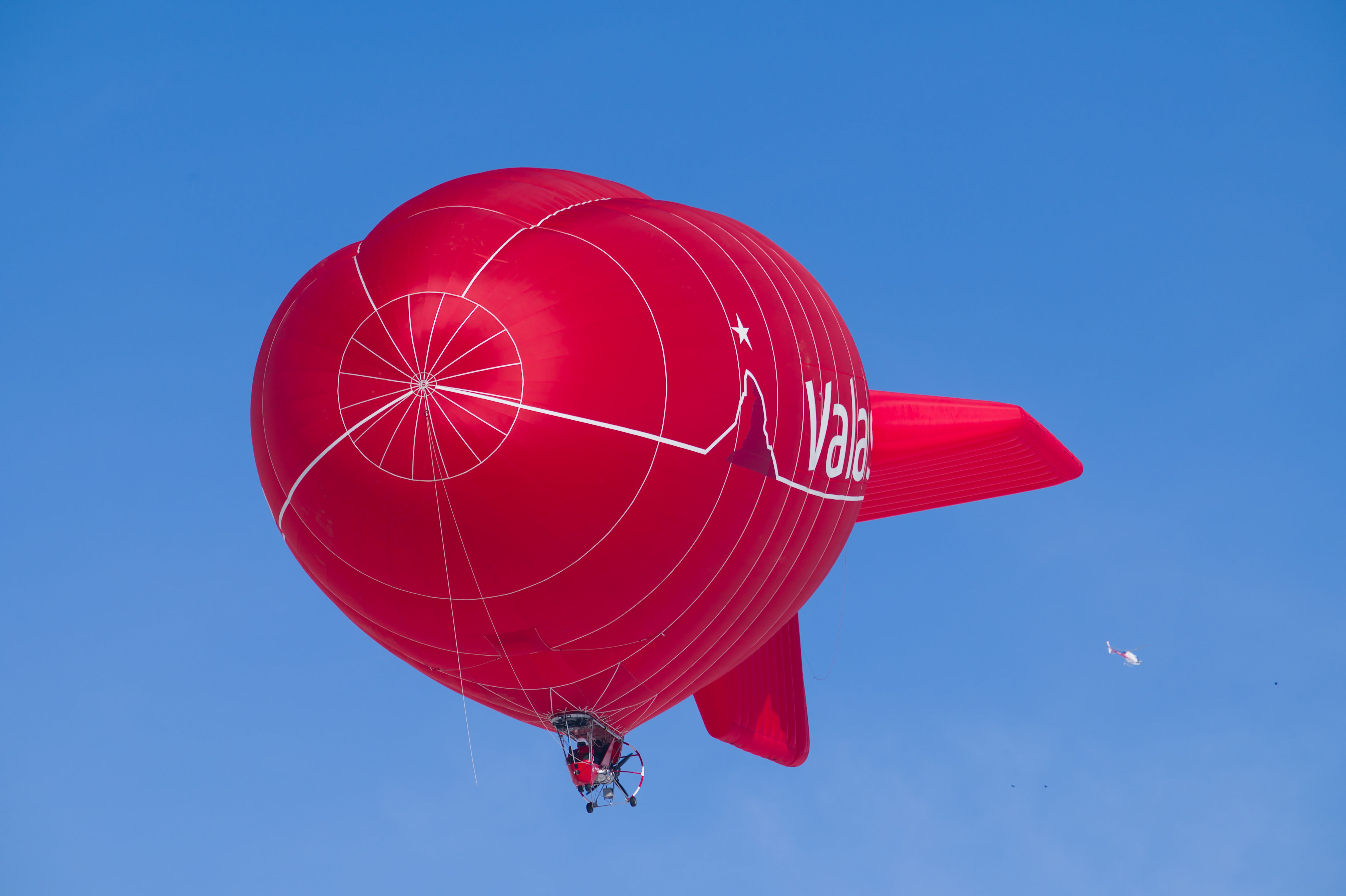 Bright red hot air balloon soaring high, showcasing vivid colors against a clear blue sky.