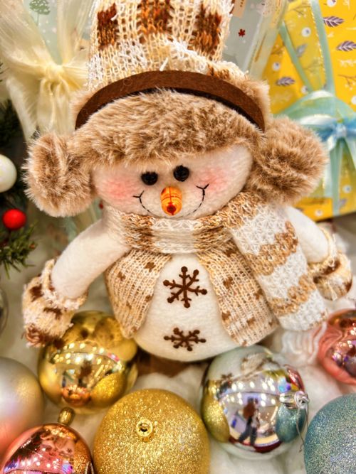 Free Cute snowman plush toy with knitted hat and scarf surrounded by festive ornaments. Stock Photo