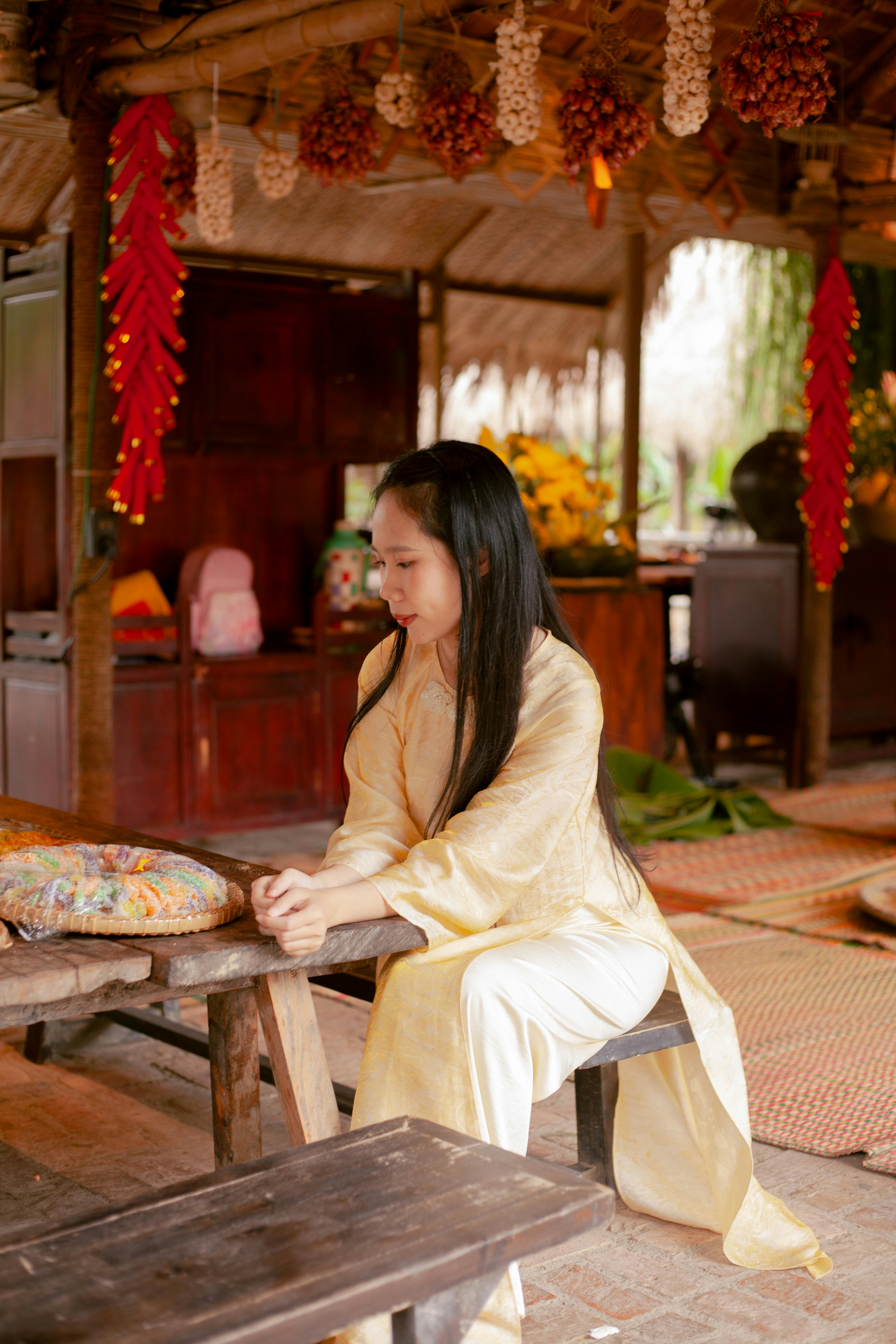Gratis Mujer asiática con atuendo tradicional sentada en un interior rústico con decoraciones vibrantes. Foto de stock