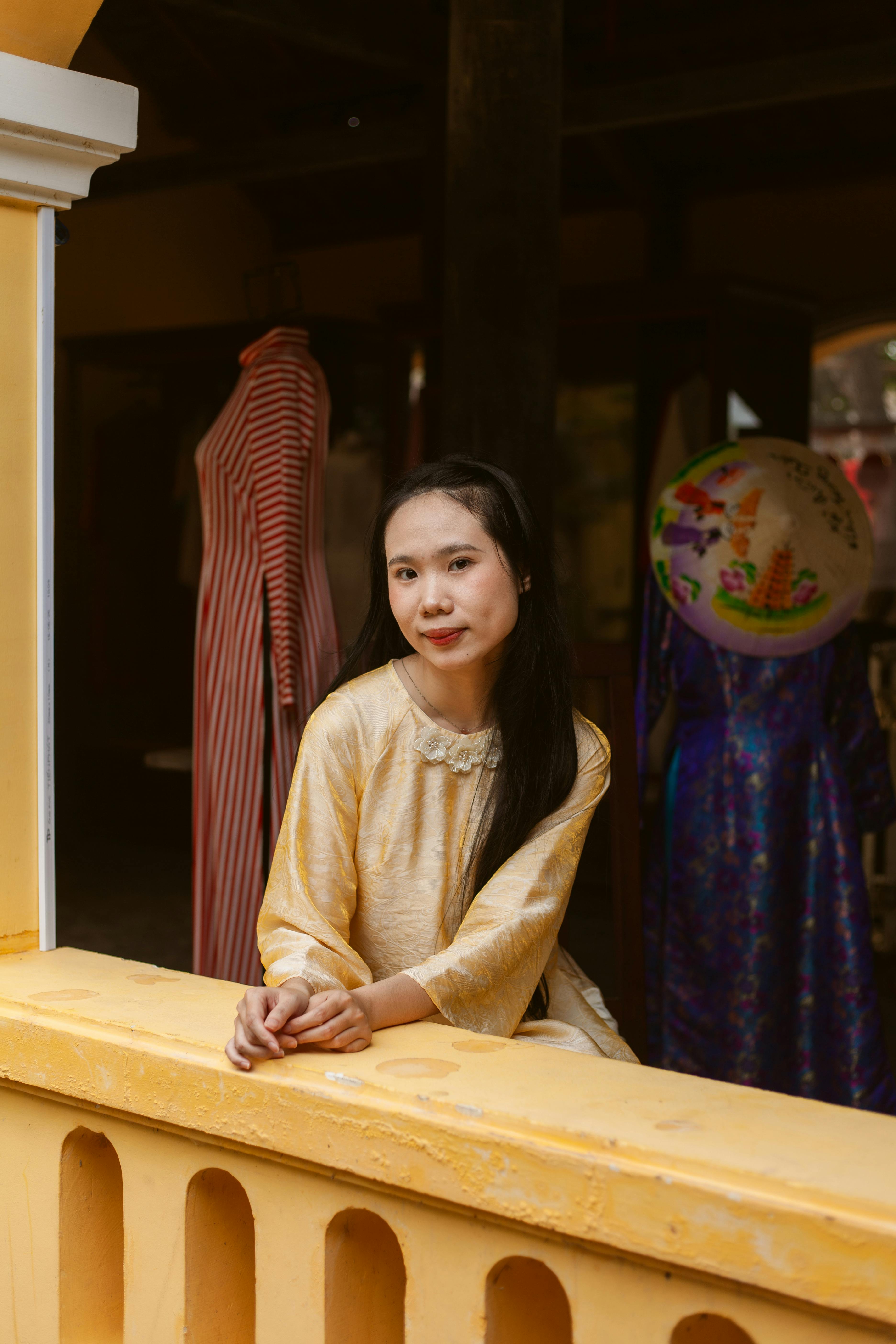 Gratis Retrato de una mujer joven con un vestido amarillo, posando elegantemente en un balcón interior. Foto de stock