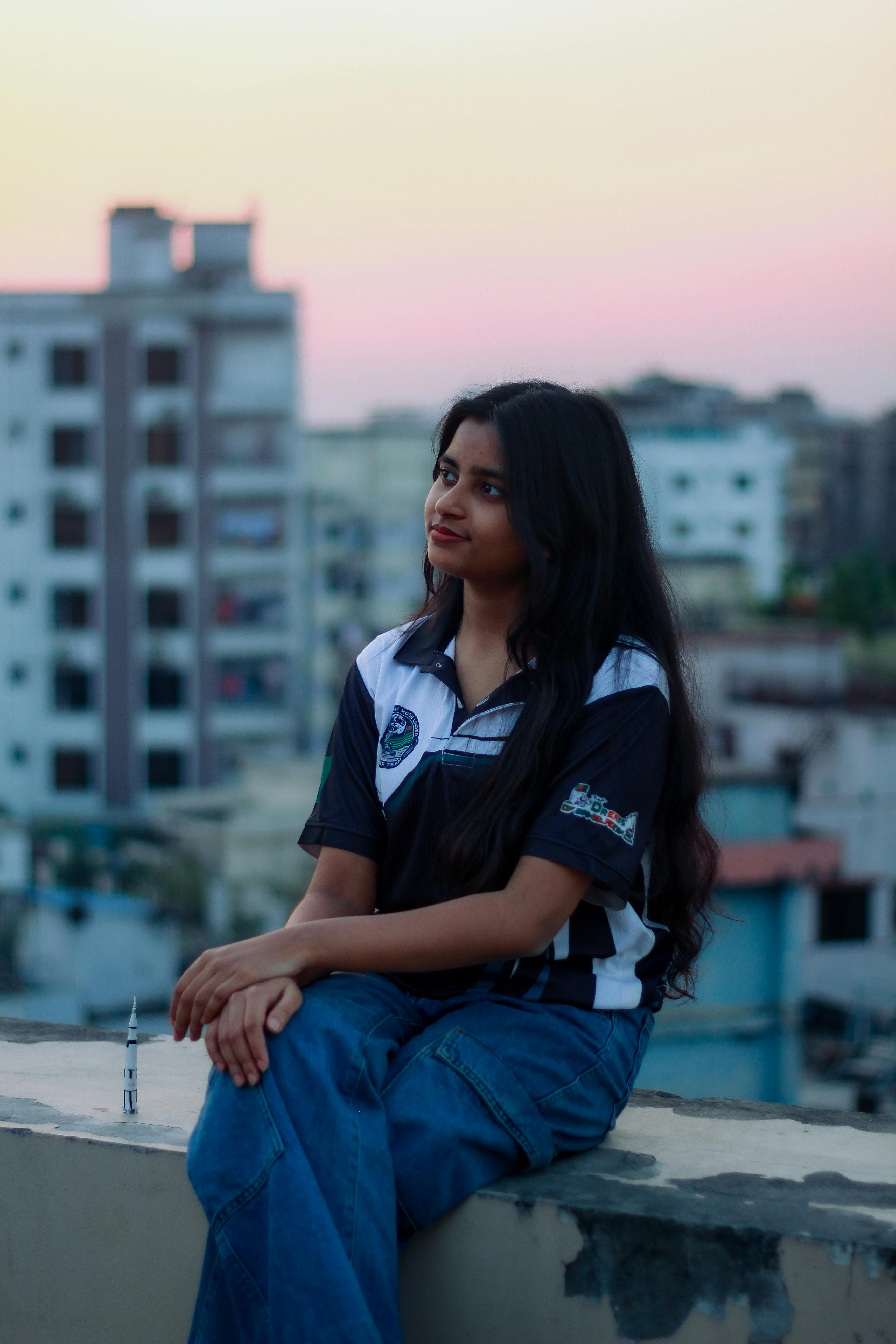 Gratis Retrato de una joven del sur de Asia sentada en una azotea en Dhaka, Bangladesh, durante una vibrante puesta de sol. Foto de stock