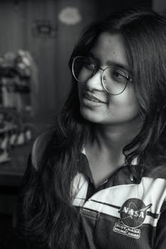 Portrait of a young woman with glasses in a NASA shirt, captured in Dhaka, Bangladesh. The image conveys a modern, inspirational feel.