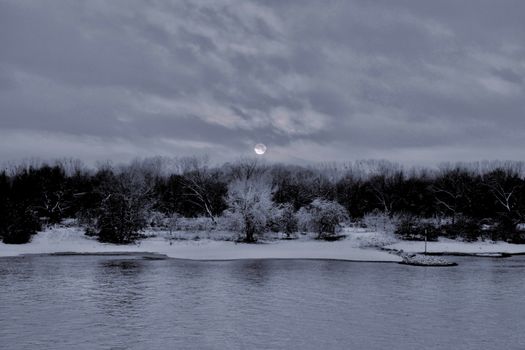 Peaceful winter scene with snow-covered trees by a river under a twilight sky.