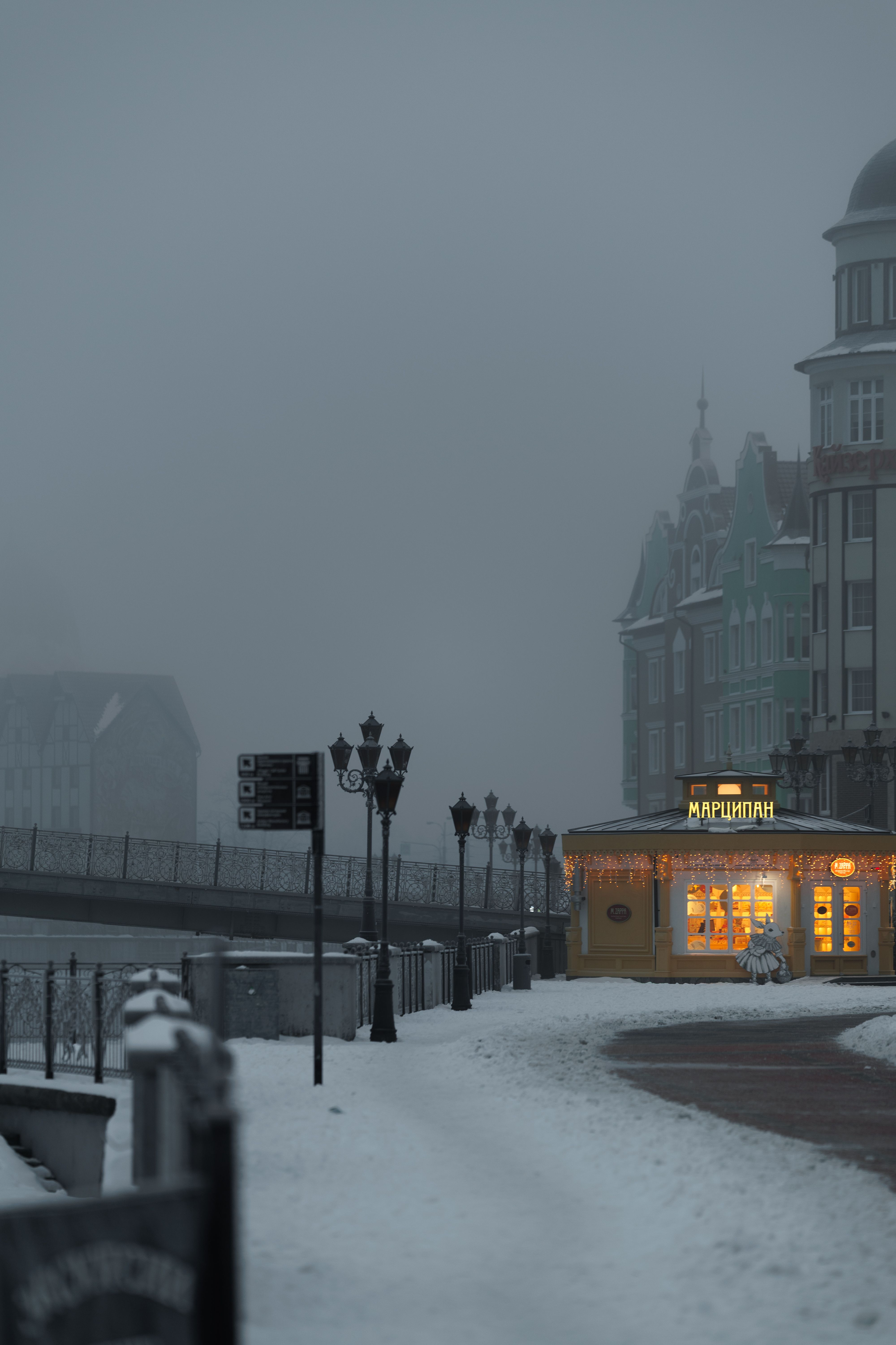 A quiet, foggy winter morning in Kaliningrad with snow-covered streets and warm lights from a kiosk.