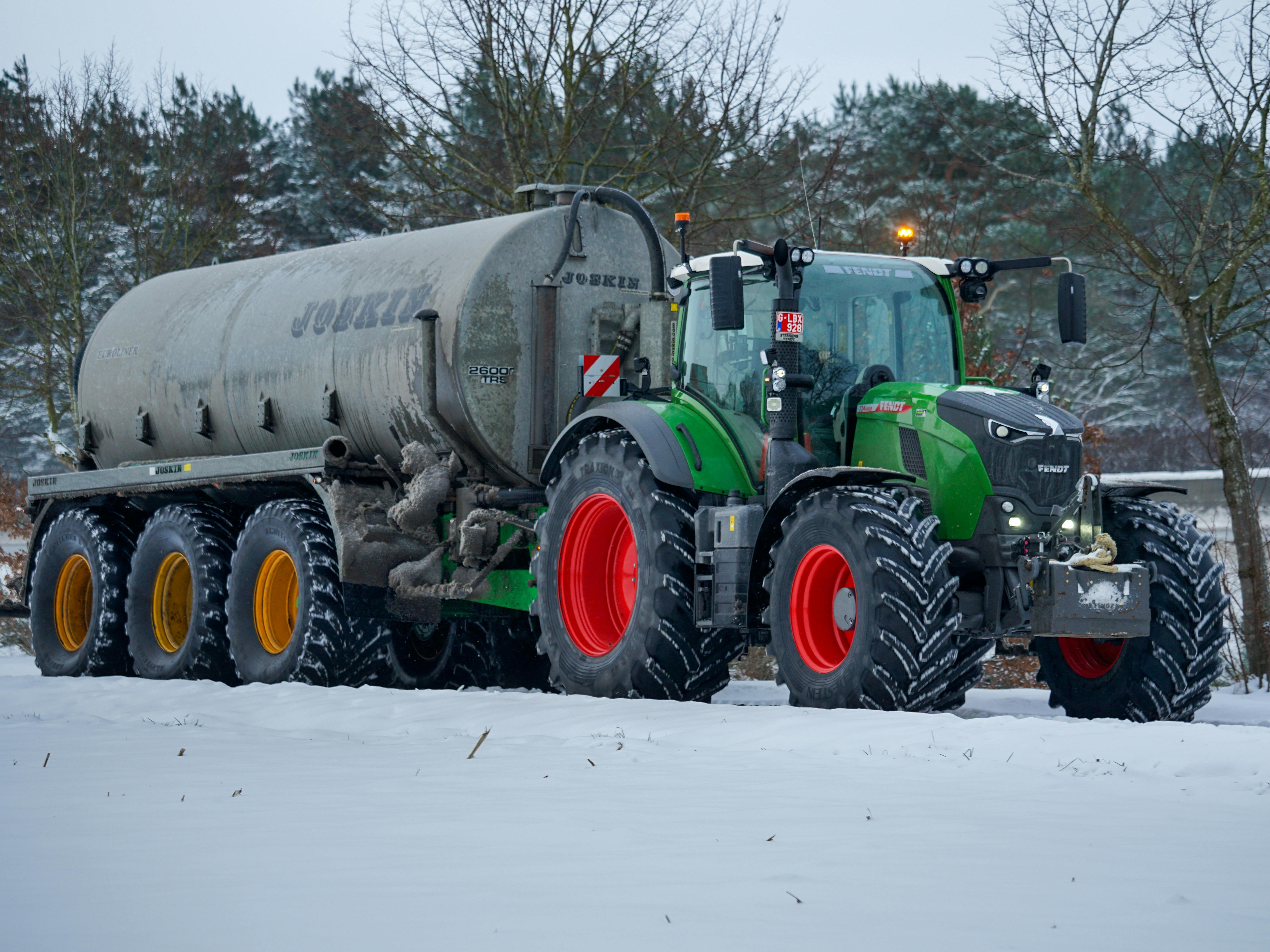 A green tractor towing a large tank in a snowy field in Retie, Belgium.