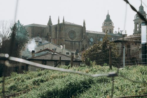 Free View of a historic church through a rustic fence, with lush greenery in the foreground. Stock Photo