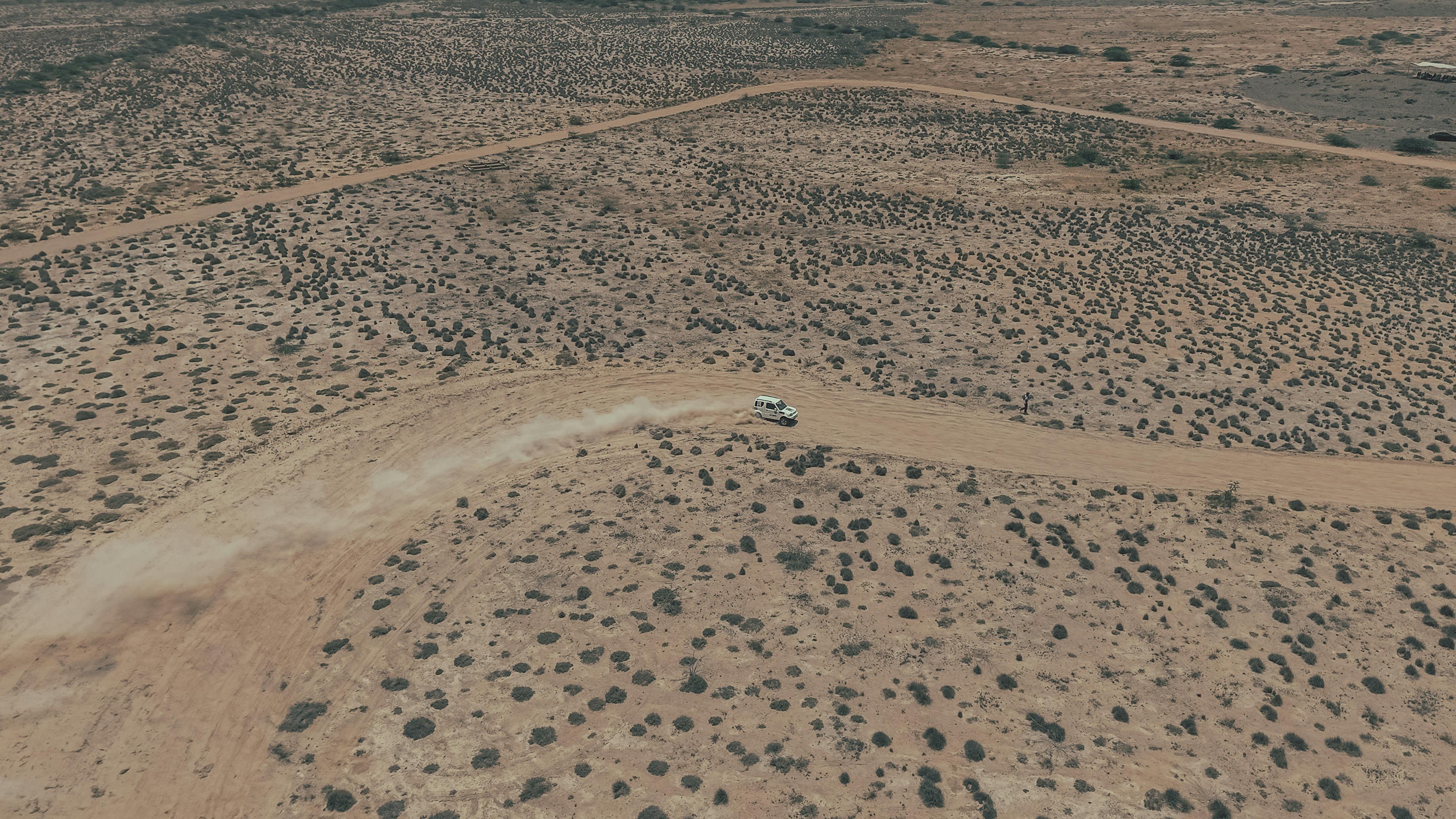 Ilmainen Pölyinen polku maastoajoneuvon kanssa laajassa aavikkomaisemassa, kuvattuna ylhäältä päin. Kuvapankkikuva