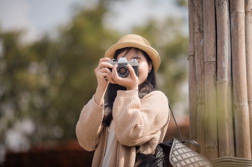 Free Young woman capturing a moment with a vintage camera outdoors, embodying style and passion. Stock Photo