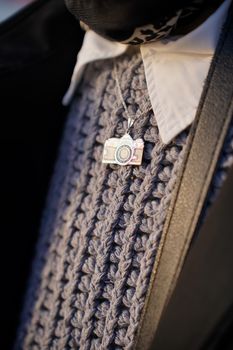 Silver camera pendant on a textured gray knit sweater with white collar.