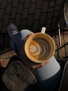 A person enjoys a latte with beautiful latte art outdoors on a sunny day.