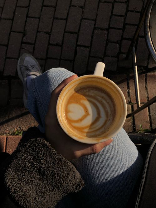 Free A person enjoys a latte with beautiful latte art outdoors on a sunny day. Stock Photo