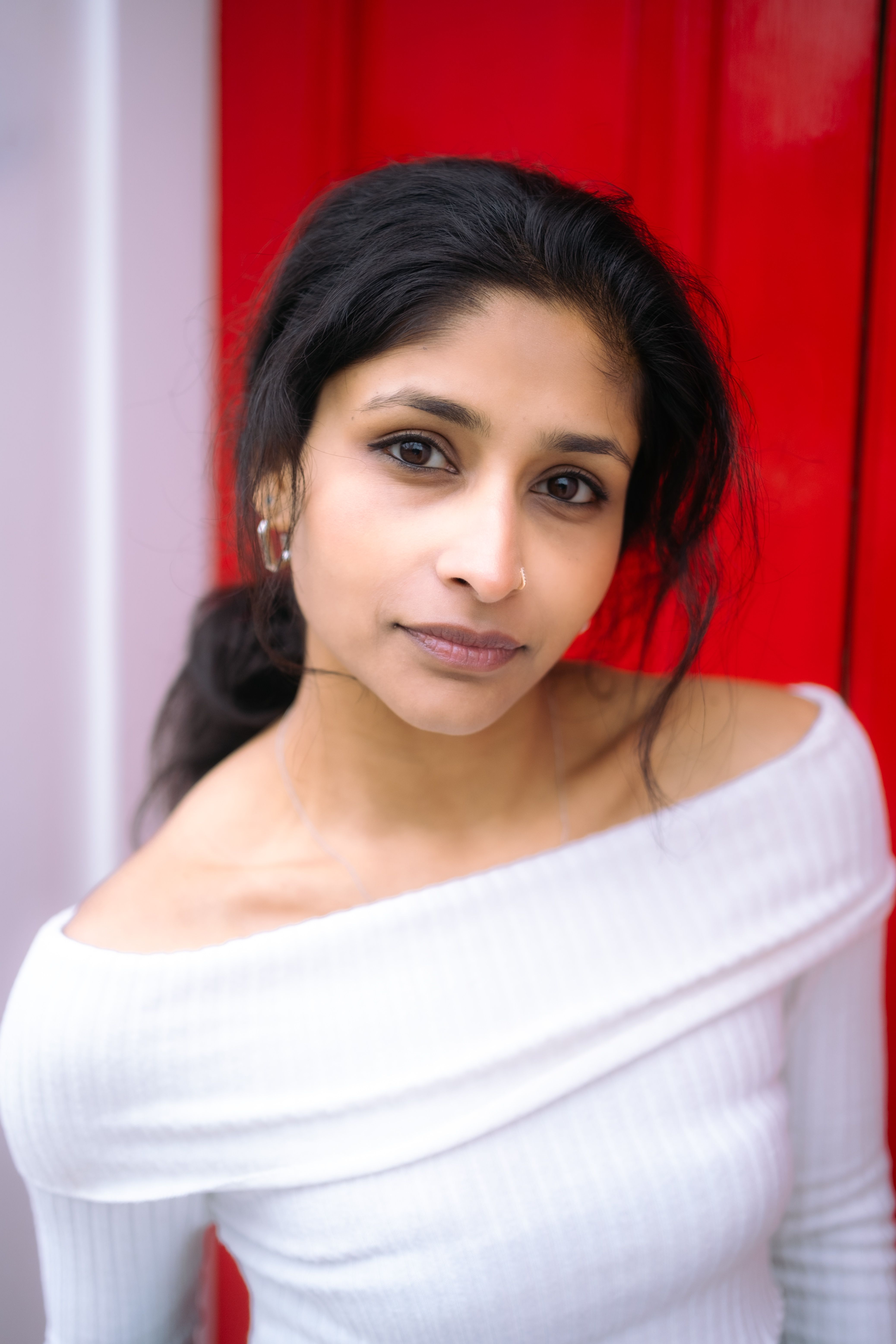 Portrait of a serene woman with expressive eyes and dark hair, wearing a white top against a vibrant red background in Dublin.