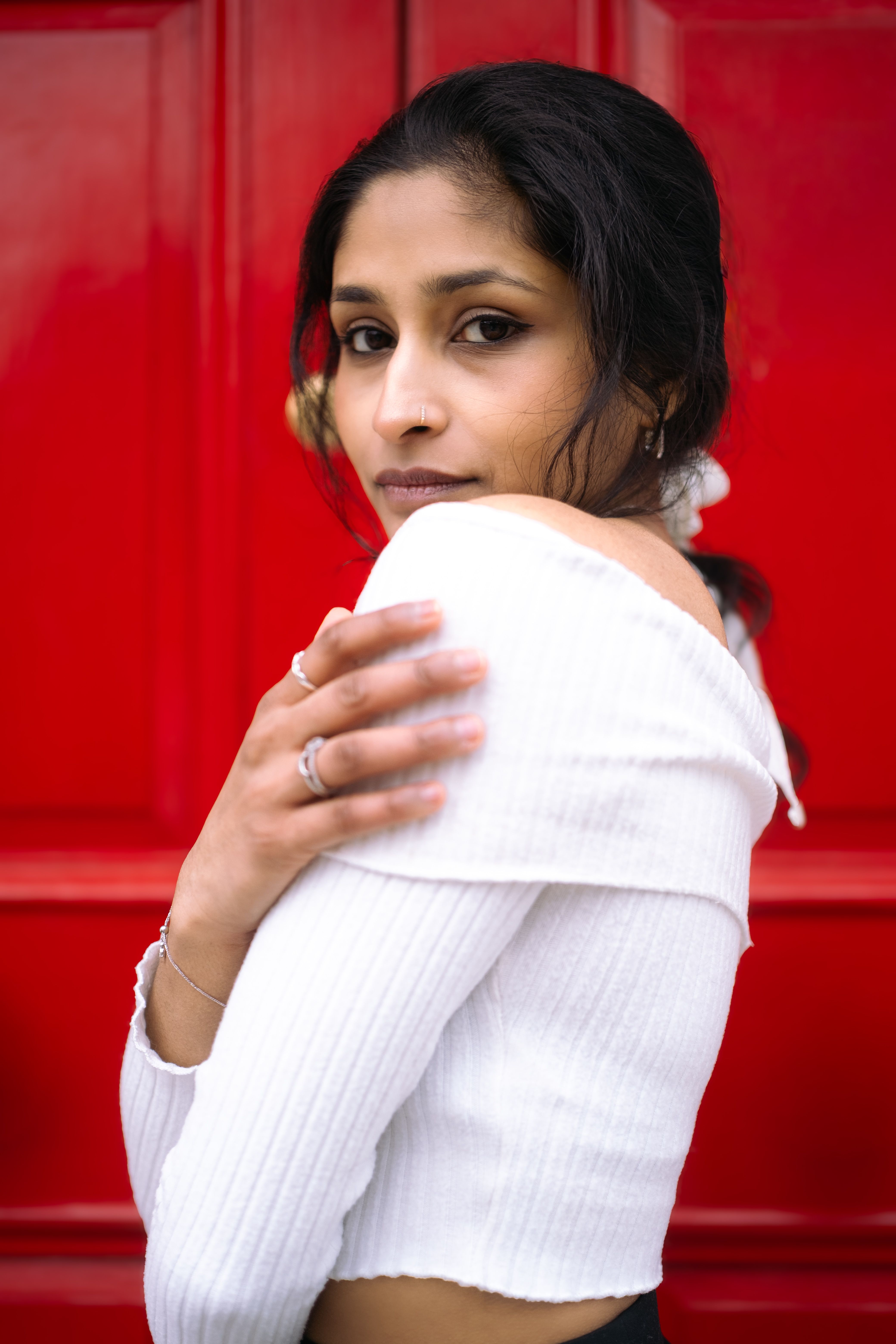 Artistic portrait of a woman with a serious expression, posing against a vibrant red door.