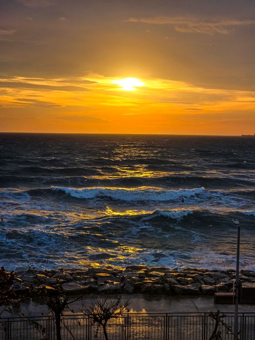 Free Captivating sunset over ocean waves with golden sky and rocky beach foreground. Stock Photo
