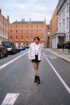 Young woman posing in stylish outfit on a Dublin street amidst urban architecture.