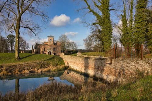 Free A rustic brick castle with a moat, surrounded by autumn trees under a blue sky. Stock Photo