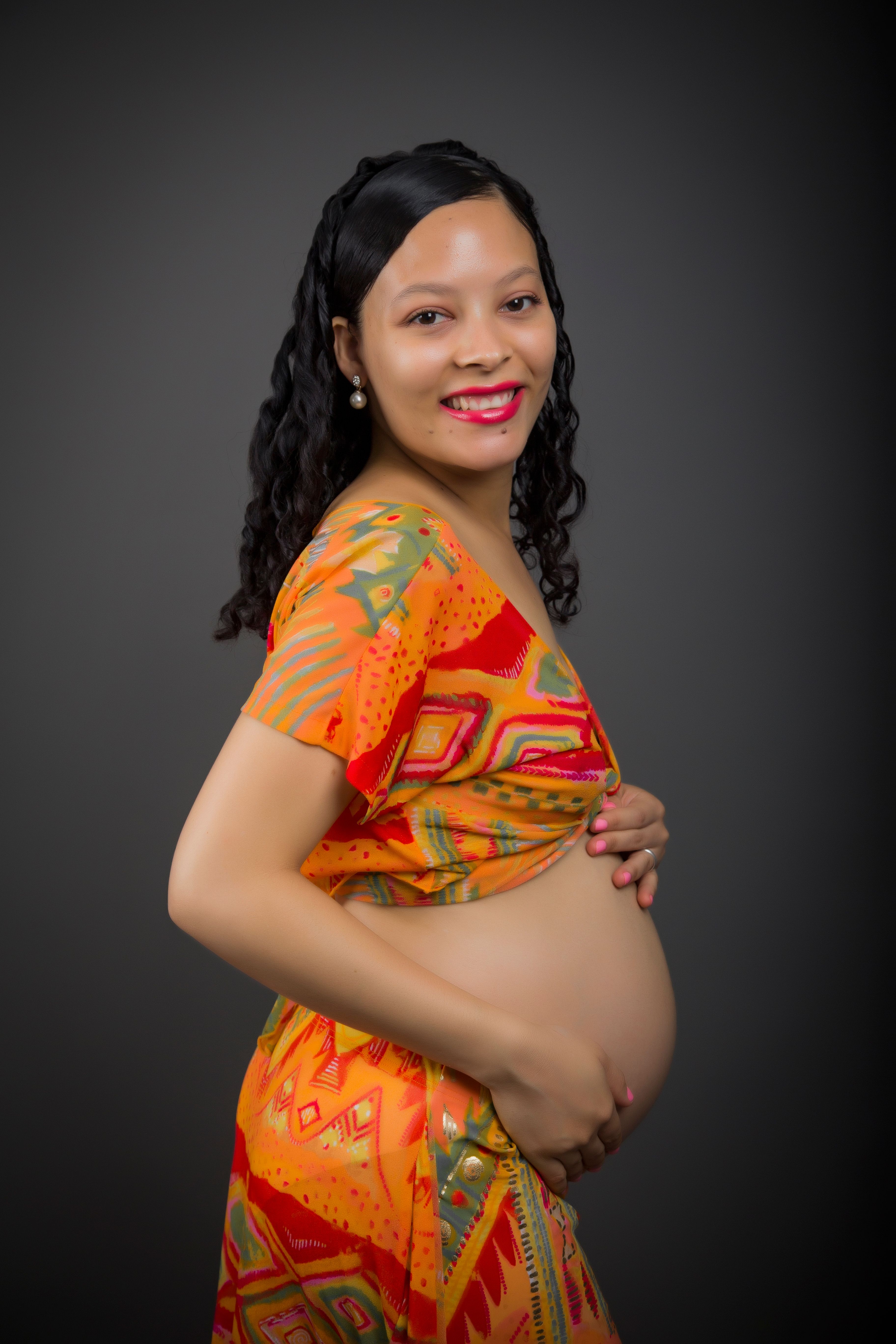 A joyful pregnant woman in colorful attire poses in a studio setting.