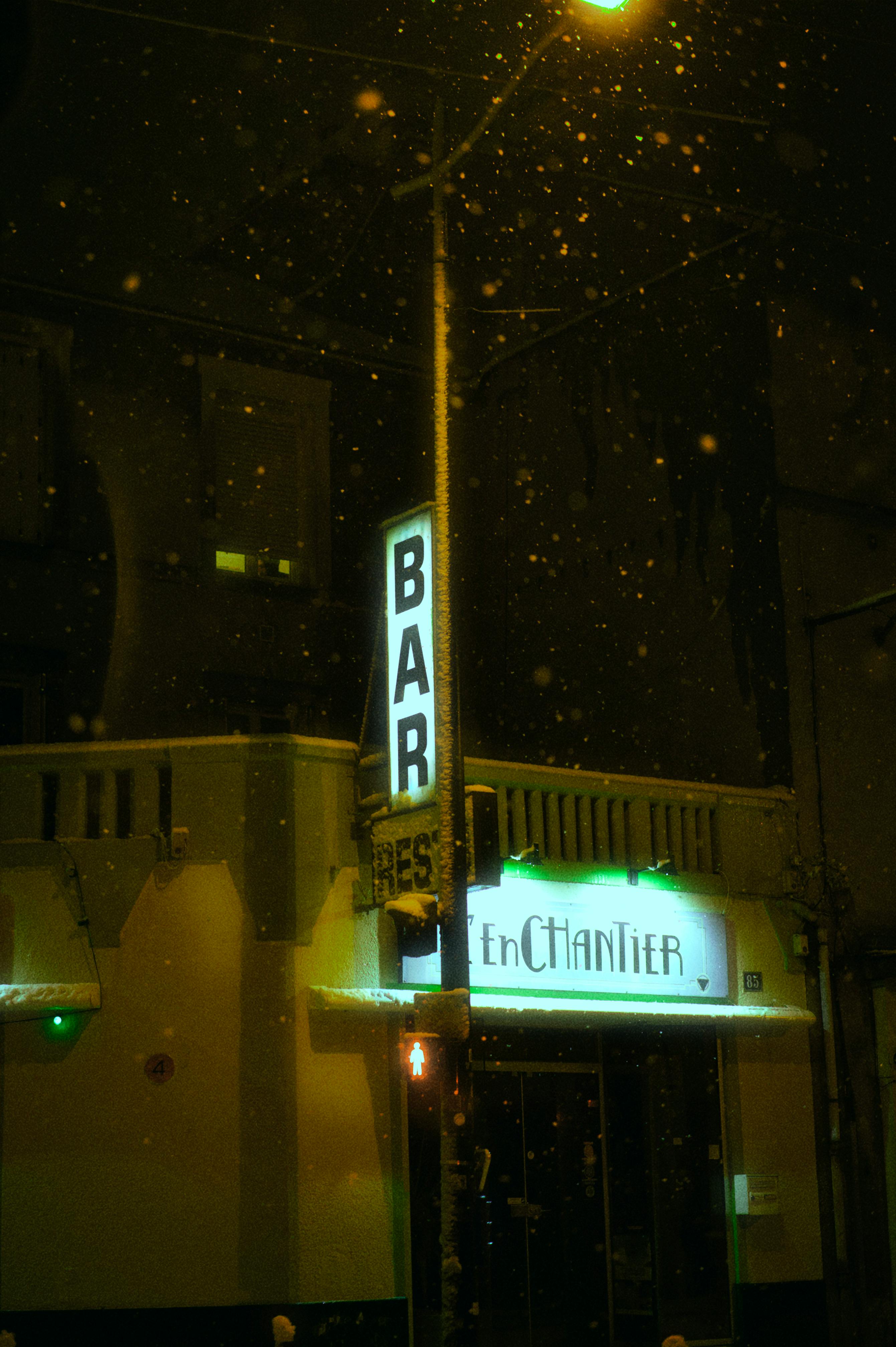 Free Warm, inviting bar entrance illuminated at night with snowflakes falling gently. Stock Photo