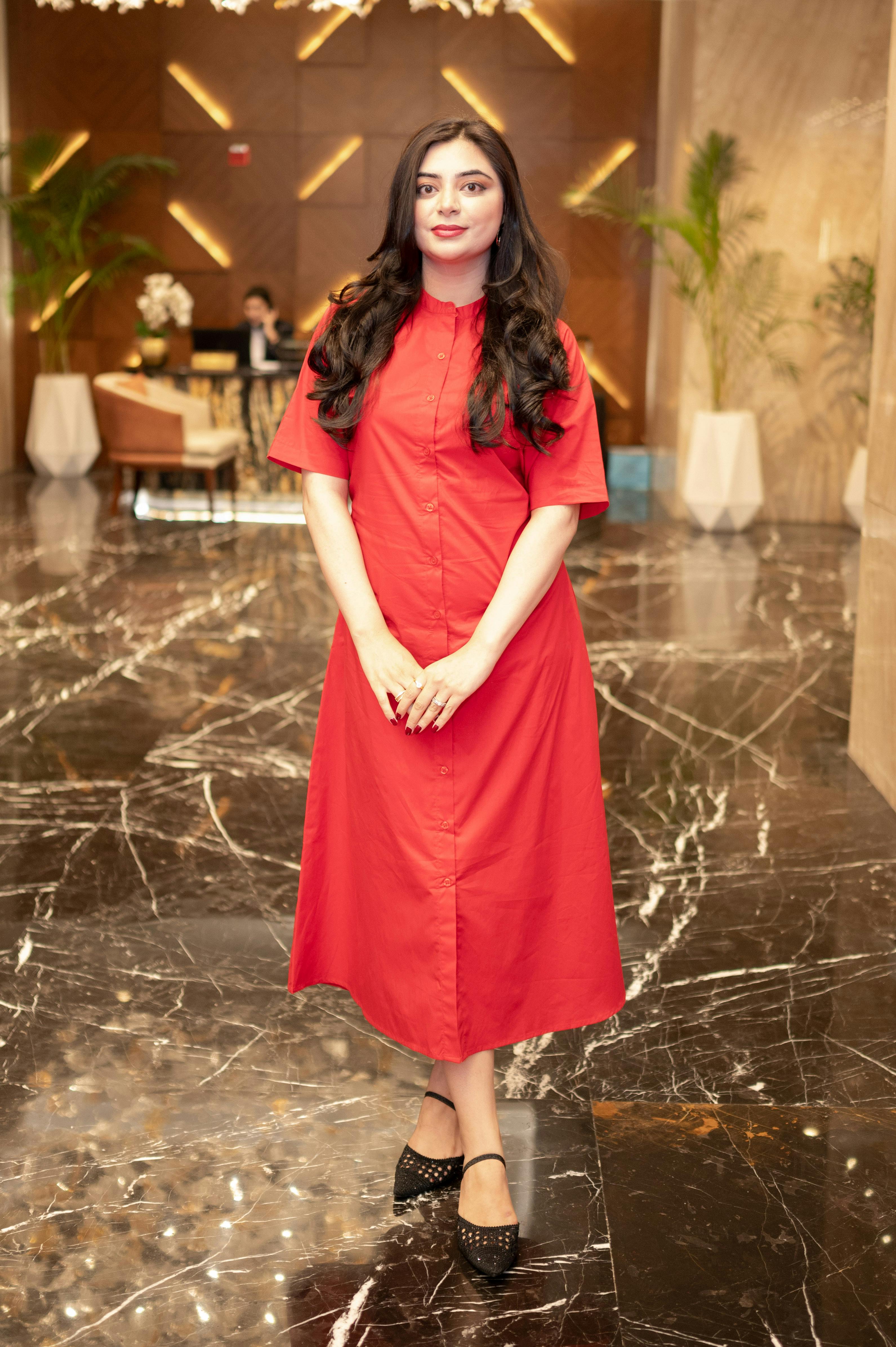 De franc Dona jove i elegant amb vestit vermell dempeus al vestíbul d'un hotel luxós. Foto d'estoc